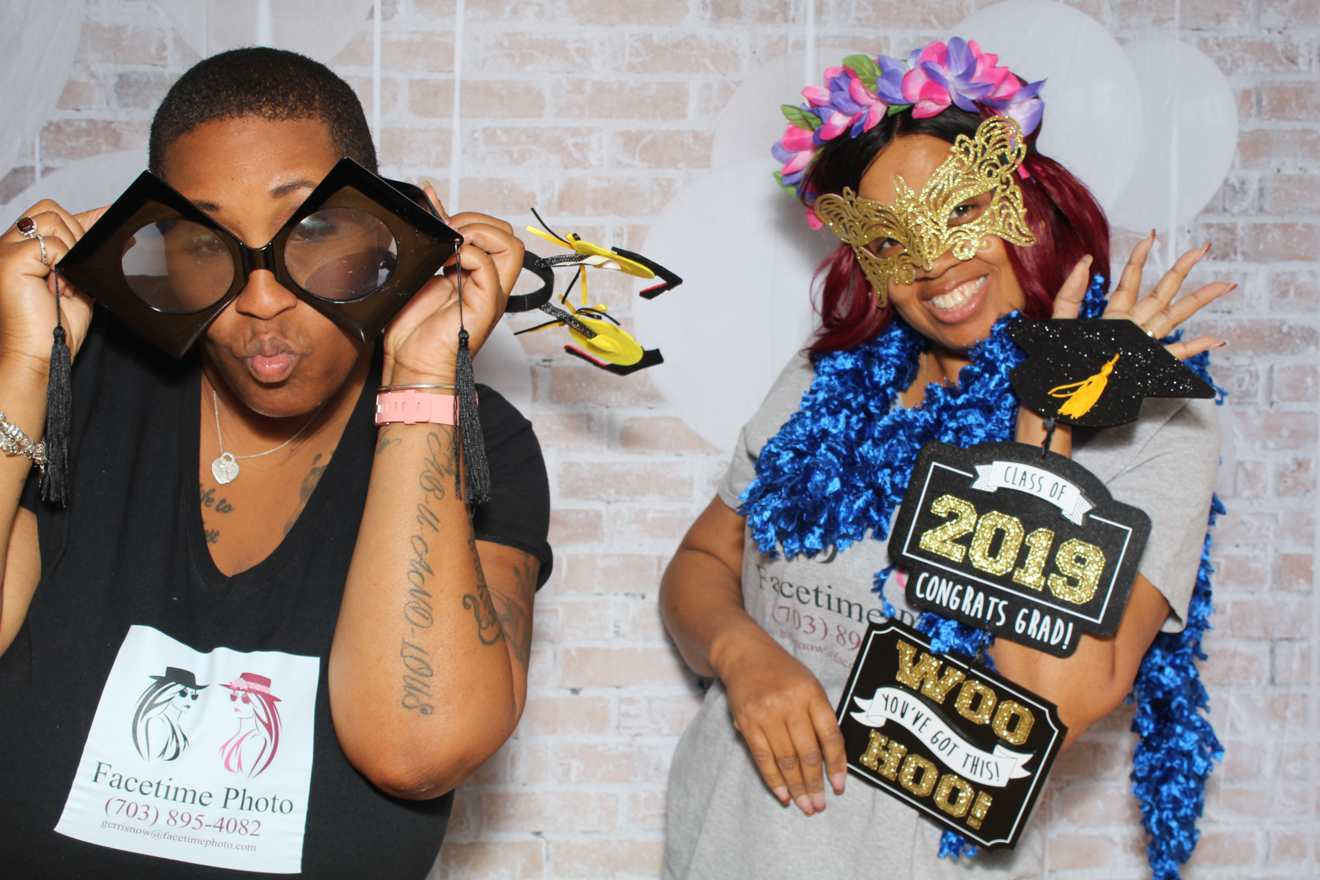 Two women posing for a picture in front of a brick wall.