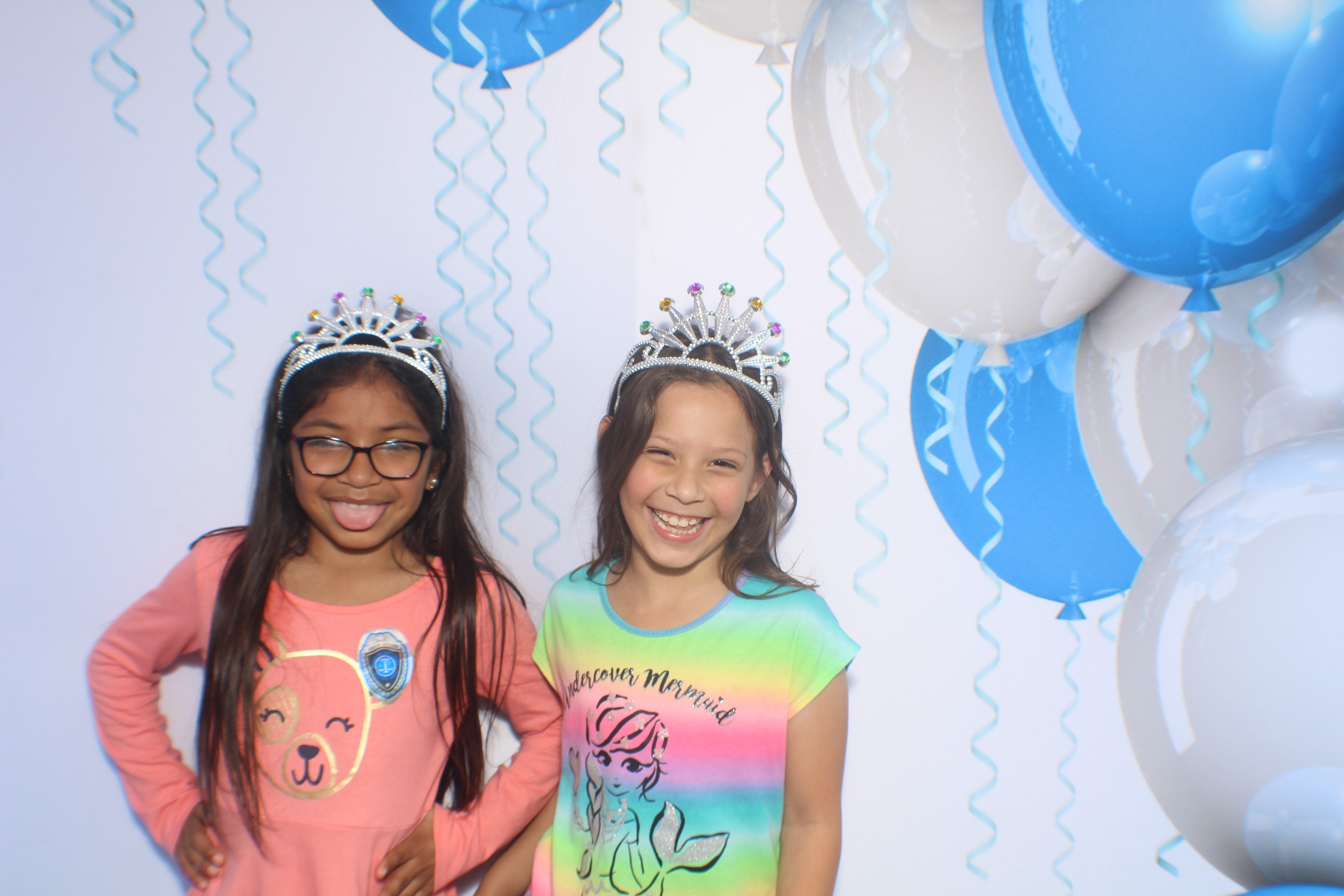 Two girls wearing tiaras and smiling for a picture.
