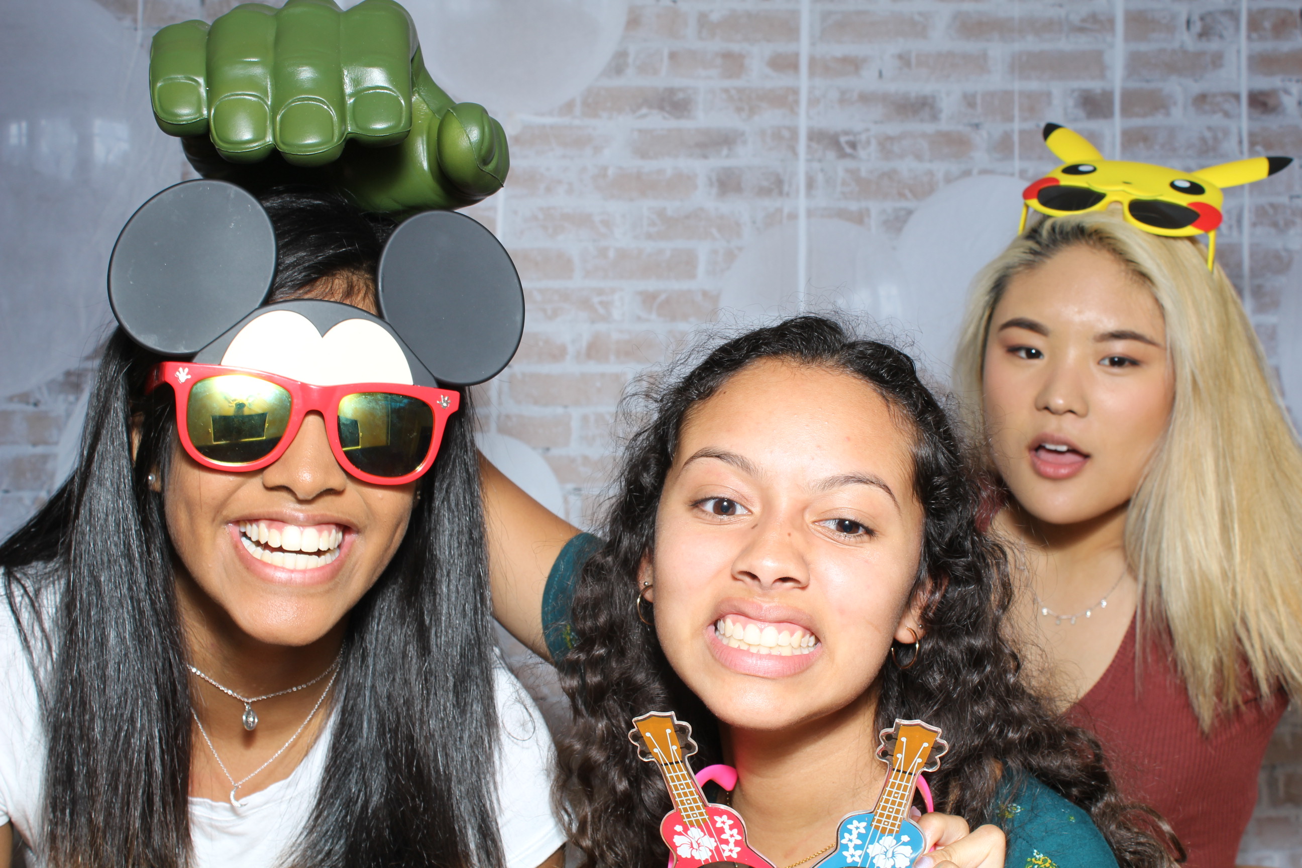 Three girls posing for a picture in front of brick wall.