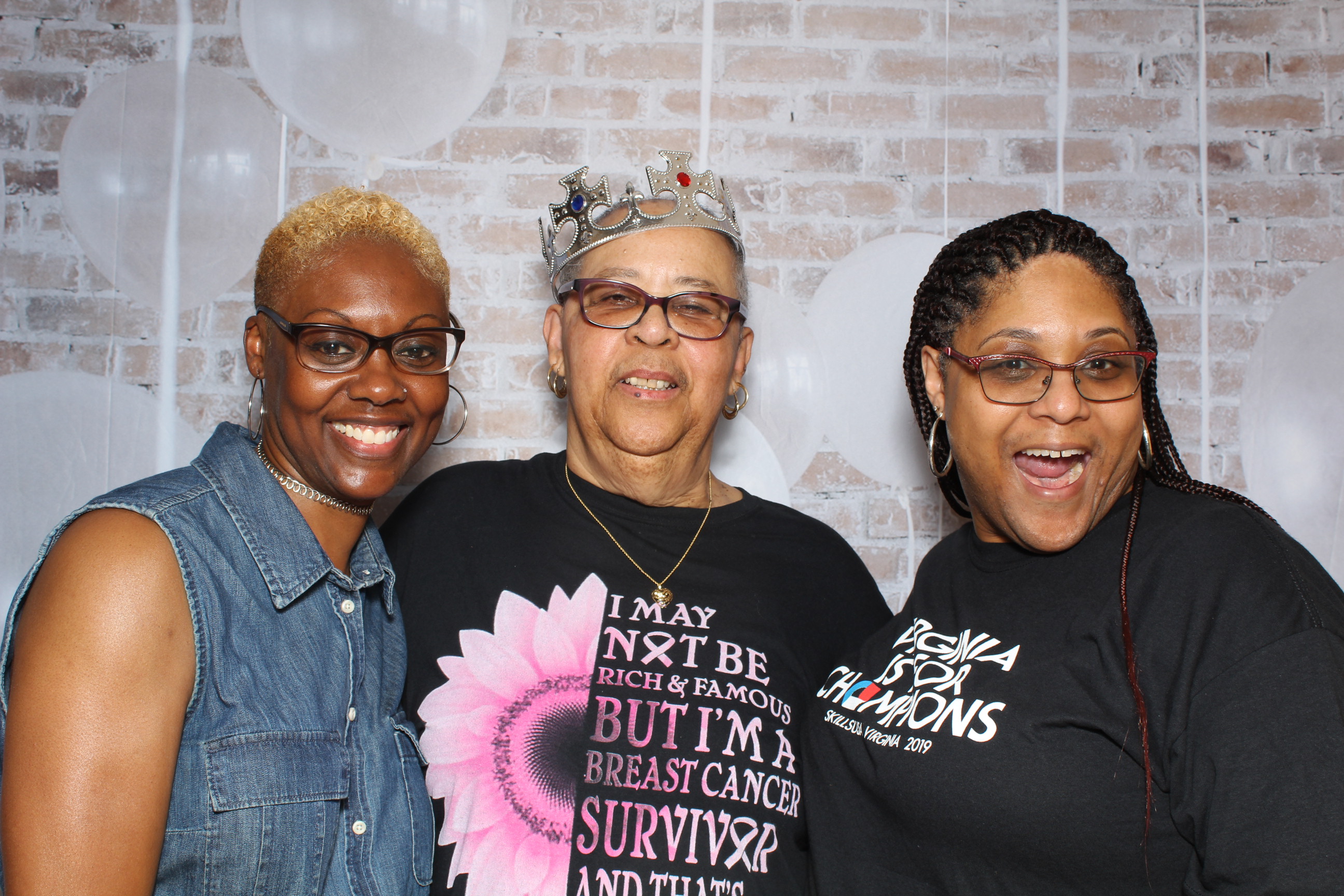 Three women posing for a picture in front of a brick wall.