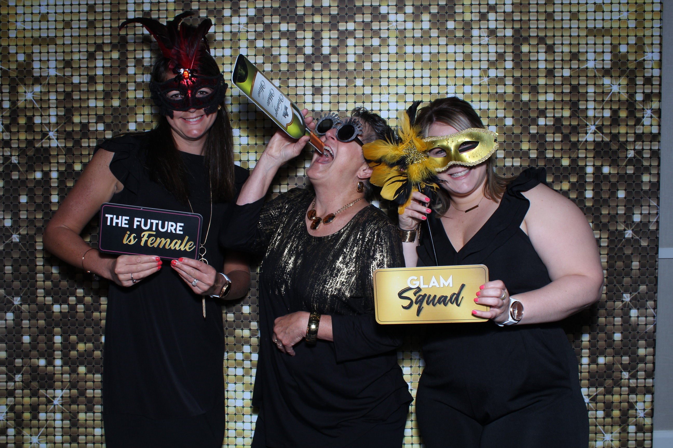 Three women wearing masks and holding signs in front of a wall.